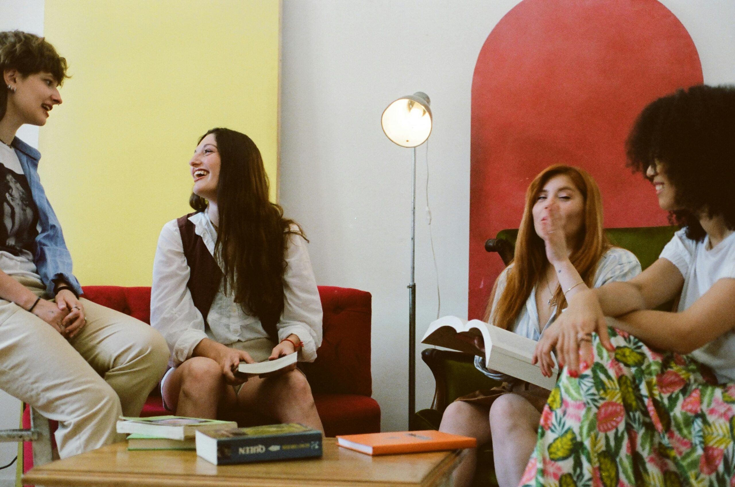 Four friends laughing and reading books in a cozy indoor setting with colorful decor.